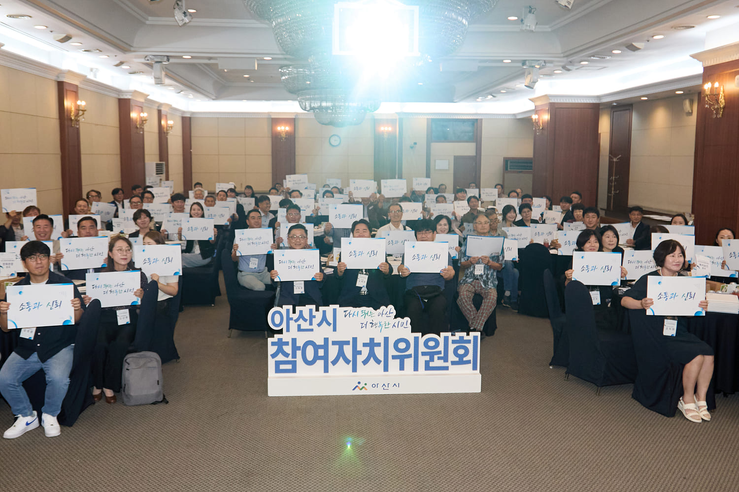 아산시 참여자치위원회 출범식에서 관객들이 각자 다른 글자가 쓰여 있는 피켓을 들고 있는 사진